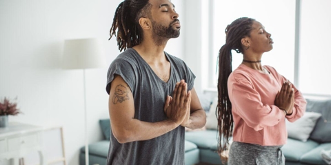 black man and woman standing with eyes clothes and holding their hands together while meditating