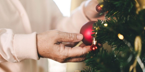older woman putting a red ornament on a christmas tree